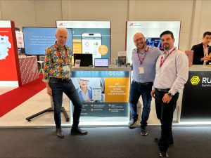 3 Personen stehen bei Messestand und präsentieren die Pflege Cloud bei der DMEA in Berlin 2024